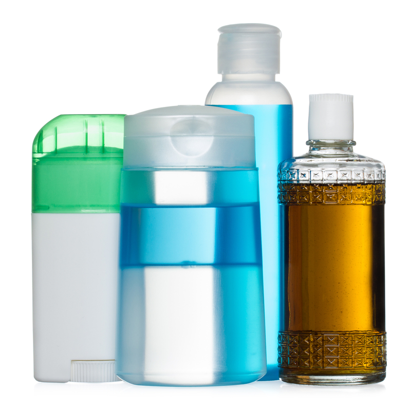 Four assorted toiletry bottles in various shapes and colors, including a green-and-white stick container, two clear plastic bottles with blue liquid, and a decorative amber glass bottle with a white cap.