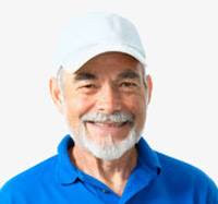 Portrait of an older man with a white beard and mustache, wearing a white baseball cap and a blue collared shirt, smiling against a plain white background.