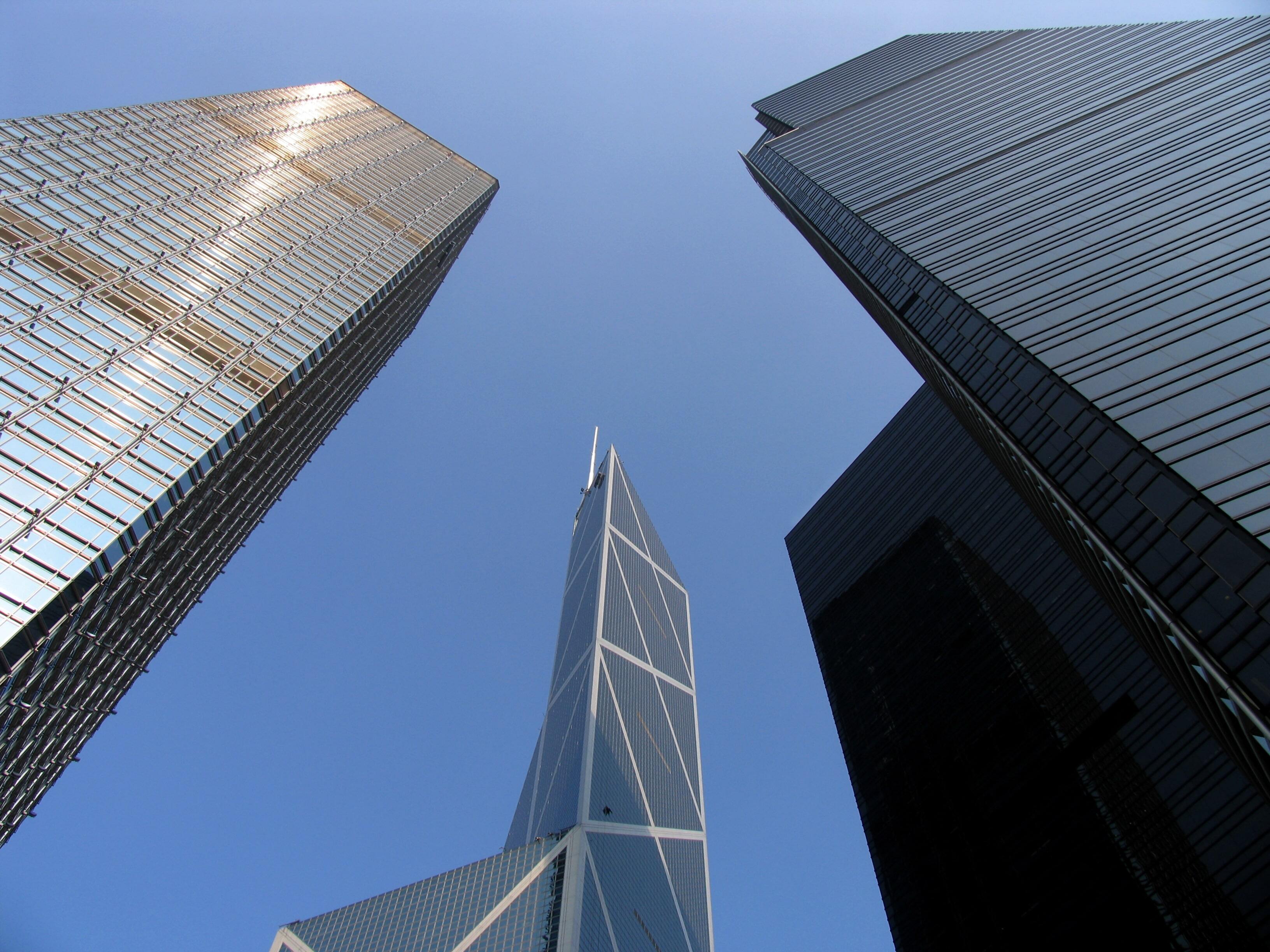 Upward view of three modern skyscrapers against a clear blue sky, converging toward the center of the image.