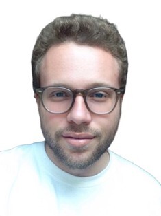 Headshot of a man with short curly hair, a trimmed beard, and round eyeglasses, wearing a white shirt and smiling slightly against a white background.