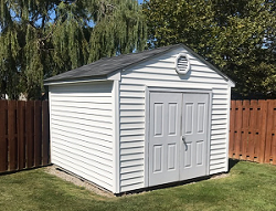 a white residential storage shed in the corner of a backyard next to a wood fence