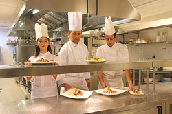 Global Foodservice Three chefs with food dishes in a restaurant kitchen
